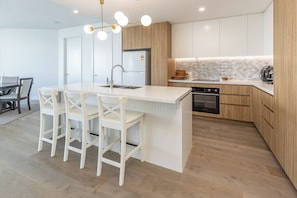 A modern kitchen with a central island, white bar stools, a built-in oven, and wooden cabinetry. - Solaris 509: 2  BR, 1  BA Apartment in Forster, Sleeps 4 (Forster)