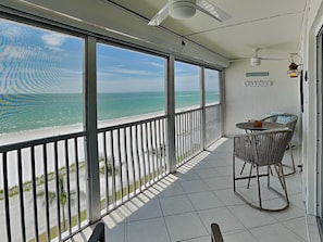 Ein Balkon mit Blick auf das Meer, einem Tisch mit Stühlen und einem Deckenventilator.
