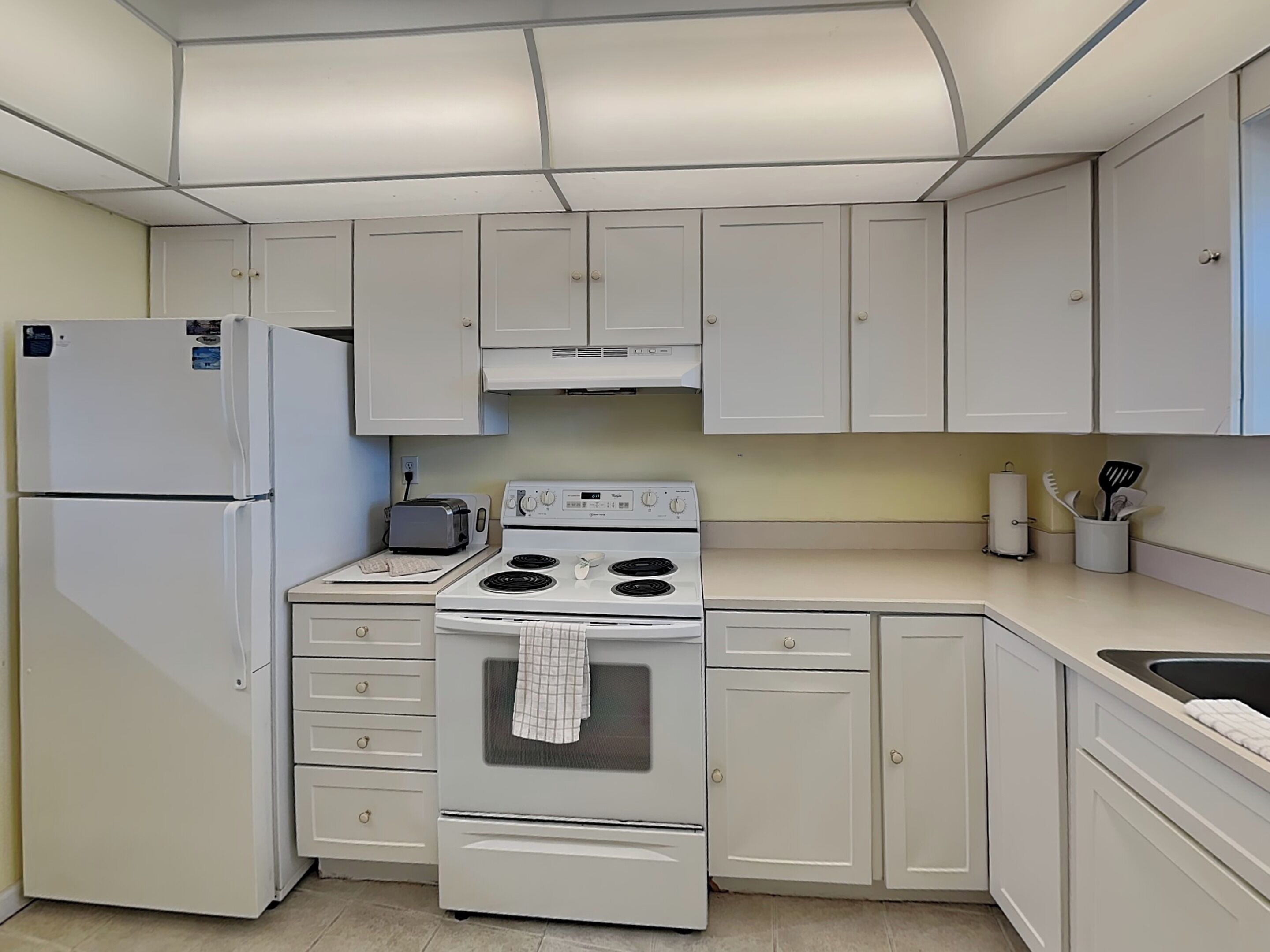 A kitchen with white cabinets, a refrigerator, a stove, a toaster, and a sink.
