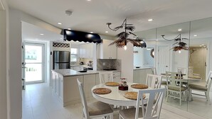 Cozinha moderna com armários brancos, uma ilha central e uma área de refeições com mesa redonda e cadeiras brancas.