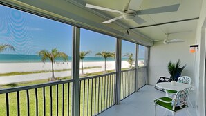 Uma varanda com vista para a praia, um ventilador de teto e uma mesa com cadeiras.