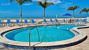 Área de piscina com espreguiçadeiras e palmeiras, céu claro e vista para o oceano.