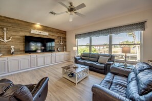 Ein Wohnzimmer mit Fernseher, Ledersofas, Couchtisch und Deckenventilator.