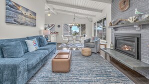 A living room with a fireplace, a sofa, a coffee table, and a dining area with a table and chairs. - Beach Nest: Modern Coastal Getaway Near Ocean, Trails & Dining (Lincoln City)