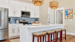 A kitchen with white cabinets, a stainless steel refrigerator, a microwave, and a large island with stools. - ☀️ Short Walk to Beach - Amazing Views - Sand Pearl ☀️ (St. Joe Beach)