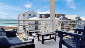 A balcony with a view of the ocean and buildings, a wooden table, and a blue sofa. - ☀️ Short Walk to Beach - Amazing Views - Sand Pearl ☀️ (St. Joe Beach)