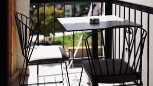 Un balcón con una mesa y dos sillas, con vista a un edificio y un árbol.