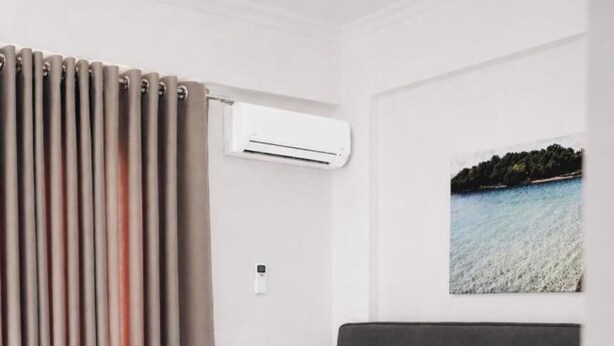 Una habitación de hotel con cama, dos mesitas de noche, un equipo de aire acondicionado y un cuadro de un paisaje costero.