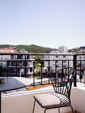 A balcony with a round table and a chair, overlooking a cityscape with buildings and a hill. - Corner Hotel (Ksamil)
