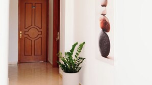 Un pasillo con una puerta de madera, una planta en maceta y un cuadro con piedras apiladas.