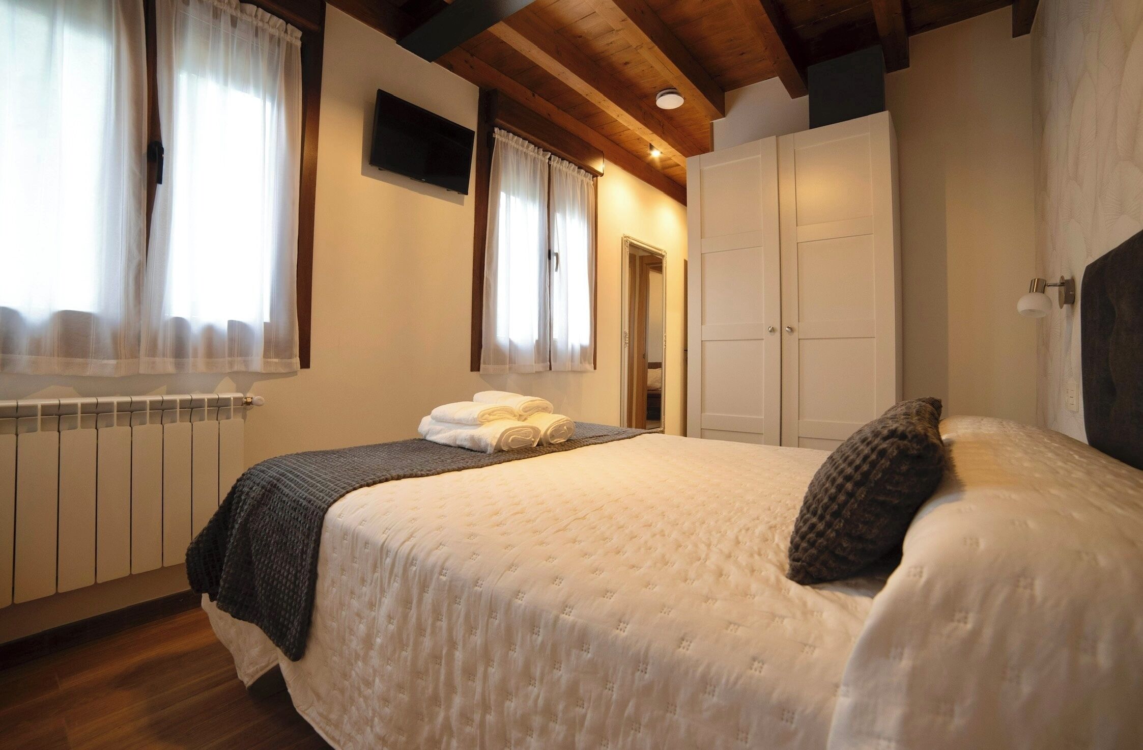 A bedroom with a bed, a radiator, a wardrobe, and a window with curtains.