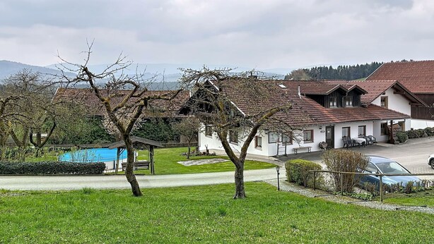 A rural setting with a white building with a red-tiled roof, a blue pool, and a car parked in front.