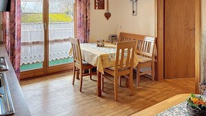 A dining area with a table set for four, wooden chairs, a clock on the wall, and a window with curtains.