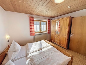 Ein Zimmer mit Bett, Holzschrank, Fenster mit Vorhängen, Heizkörper und einer Lampe.