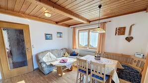 Une pièce chaleureuse avec un plafond en bois, un canapé, une table à manger avec des chaises et une fenêtre avec des rideaux.