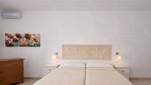 Un letto matrimoniale con testiera, due comodini con lampade, una cassettiera in legno e un condizionatore d'aria a parete.