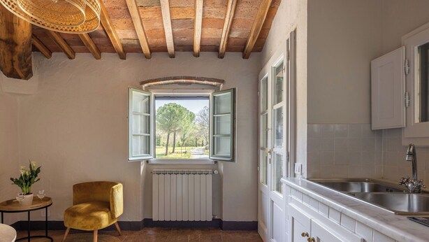 A kitchen with white cabinets, a stainless steel sink, a window with green shutters, a radiator, and a yellow chair. - Lovely apartment for 3 guests with pool, WIFI, close to Greve In Chianti (Badia A Passignano)