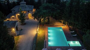 Una piscina con sillas de descanso y sombrillas, rodeada por un patio de ladrillo y un edificio de piedra.