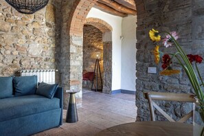 Ein rustikaler Raum mit einer Steinwand, einem Holztisch, einem blauen Sofa und einem roten Sessel.