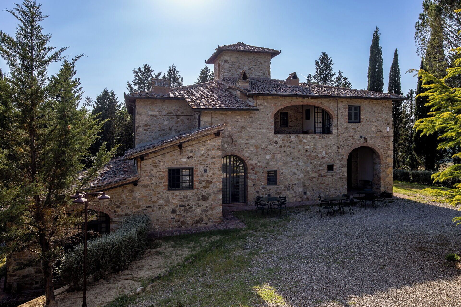 Un bâtiment en pierre avec un toit en pente, des fenêtres en arc de cercle et une cour recouverte de gravier.