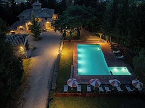 Ein Swimmingpool mit Liegestühlen und Sonnenschirmen, umgeben von einer Pflasterterrasse und einem Steinhaus.