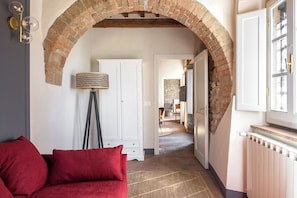 Ein Interieur mit einem roten Sofa, einer Stehlampe, einem weißen Schrank und einem Ziegelbogen, der in einen anderen Raum führt.
