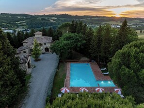Ein Pool mit Sonnenschirmen, ein Steinhaus und Blick auf die umliegenden Hügel.