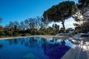 Ein klares Schwimmbecken mit Liegestühlen, umgeben von Bäumen und blauem Himmel.