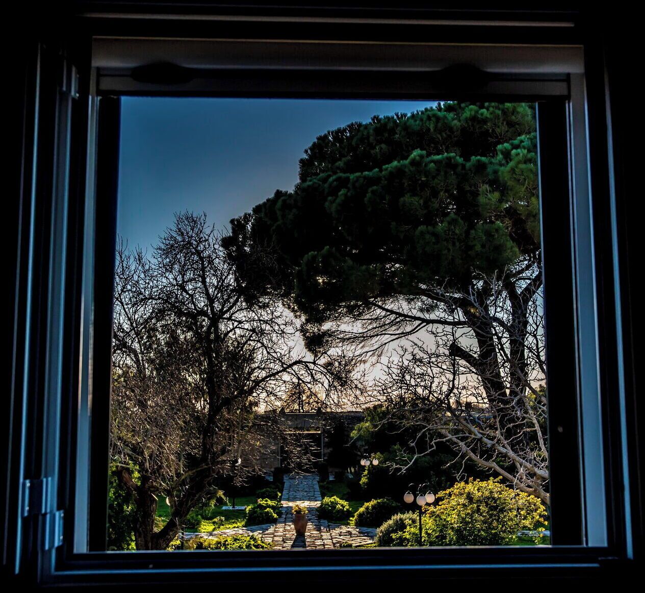 Une vue à travers une fenêtre sur un jardin avec un sentier de pierre, des arbres et un pont.