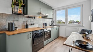 Eine moderne Küche mit integrierten Geräten, eine Essecke mit Tisch für zwei Personen und ein Fenster mit Blick auf die Stadt.