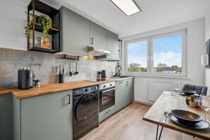 Eine moderne Küche mit integrierten Geräten, eine Essecke mit Tisch für zwei Personen und ein Fenster mit Blick auf die Stadt.