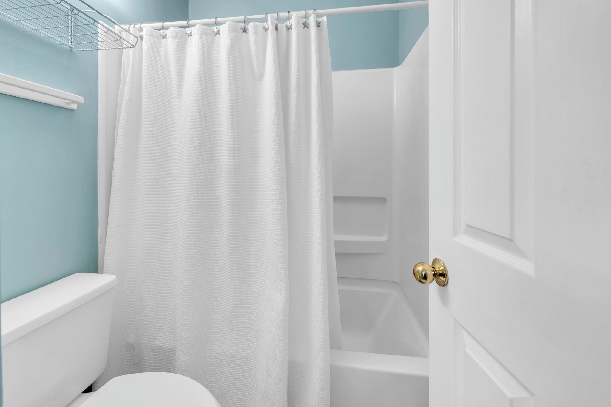 Een badkamer met een wit toilet, een douchegordijn en een witte deur met gouden handvat.
