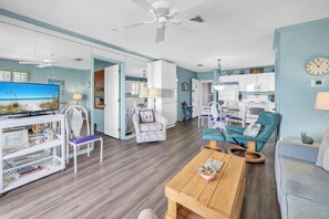 A spacious living area with a television, white wicker furniture, a wooden coffee table, and a teal armchair. - Bayfront Escape | Poolside Condo | Beach Access Across the Street (Fort Walton Beach)