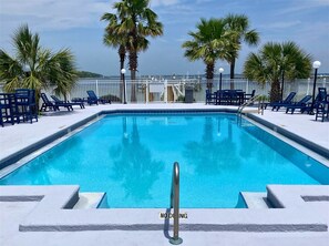 A swimming pool with a 'NO DROWNING' sign, surrounded by palm trees and blue lounge chairs. - Bayfront Escape | Poolside Condo | Beach Access Across the Street (Fort Walton Beach)