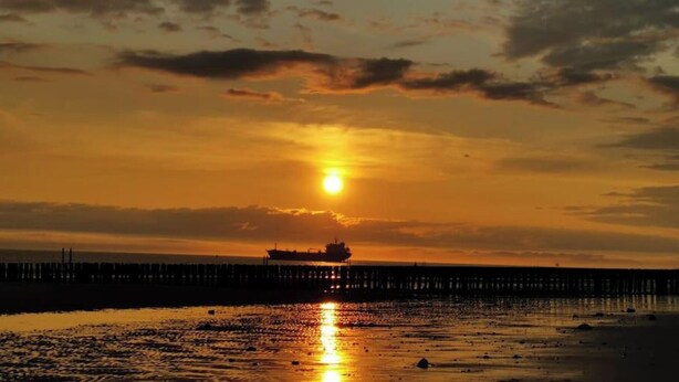 Un atardecer sobre un muelle con un barco amarrado al final.