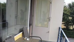 Un balcón con dos sillas de mimbre, una mesa, un ventanal de vidrio y vistas a zonas verdes.