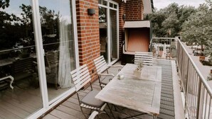 Un balcon avec une table en bois, deux chaises blanches et un fauteuil en osier.