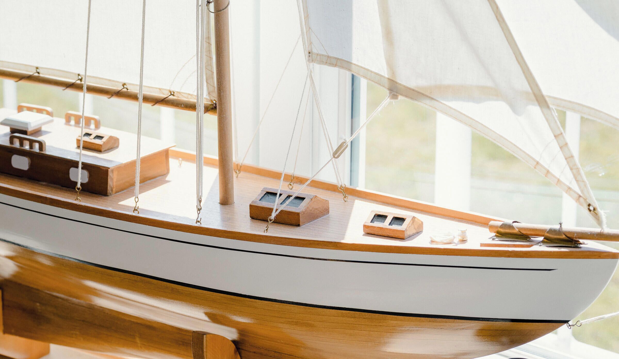 A model sailboat with a wooden deck, a white hull, and a simple cabin structure.