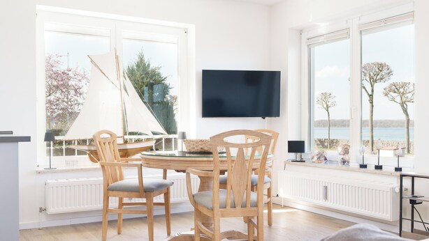 Ruokailutila, jossa on pöytä, tuoleja, purjevene ulkona ja televisio seinällä.
