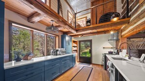 Une cuisine moderne avec des poutres en bois, de grandes fenêtres et une vue sur l’extérieur.