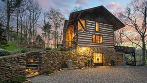 Une cabane en rondins avec un mur en pierre, un foyer et une terrasse en bois.