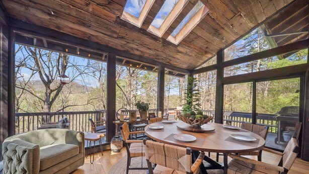 Un espace de restauration en plein air avec une table et des chaises en bois, un canapé rembourré et une vue sur les arbres et les montagnes.