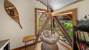 Une pièce avec un fauteuil suspendu, une petite table, une bibliothèque et une vue sur la verdure à l’extérieur.