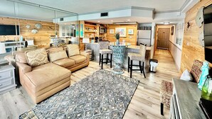 Ein modernes Wohnzimmer mit einer Couch, einem Couchtisch und einer Küchenzeile mit einer Theke und Stühlen.