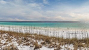 Ein Strand mit klarem türkisblauem Wasser, weißem Sand und vereinzelter Vegetation.
