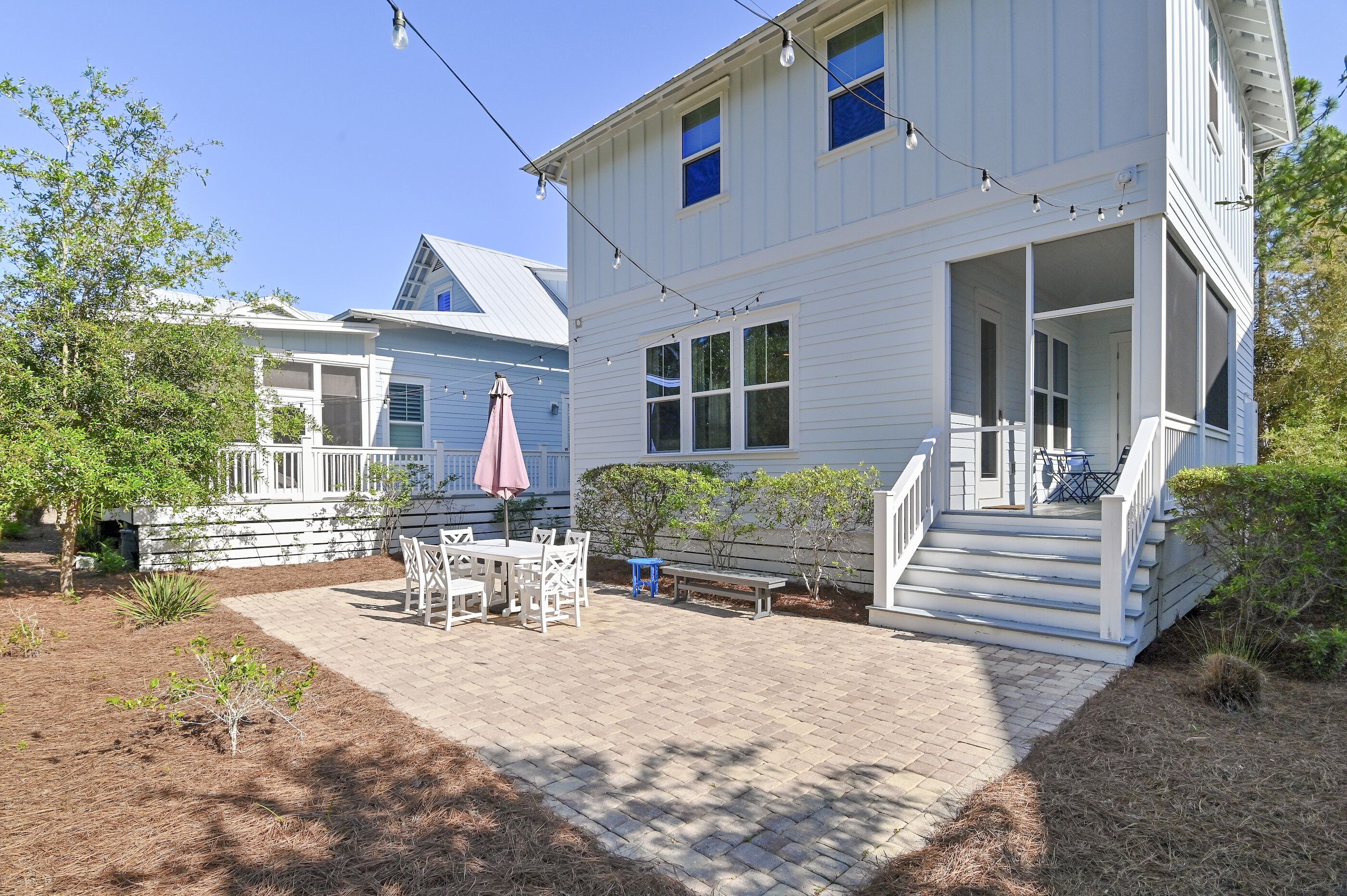 A two-story house with a porch, a table with chairs, and a string of lights.