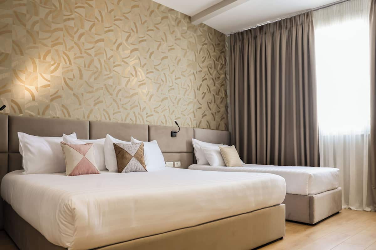 A hotel room with a large bed, a smaller bed, a nightstand, and a wall-mounted lamp.