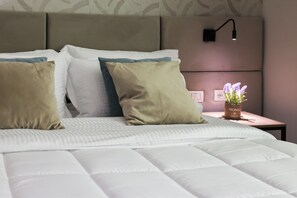 A neatly made bed with white and beige pillows, a bedside table with a potted plant, and a wall-mounted light fixture. - Best Western Plus The Met Tirana Hotel (Kashar)