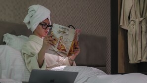 Eine Person liest ein Magazin im Bett, neben einem Laptop.