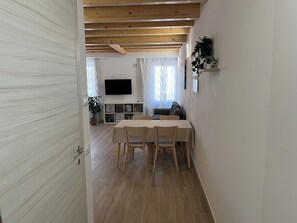 A room with a wooden ceiling, a dining table with chairs, a television on the wall, and a plant on a shelf. - Anfite Apartments Santa Maria (Desenzano del Garda)